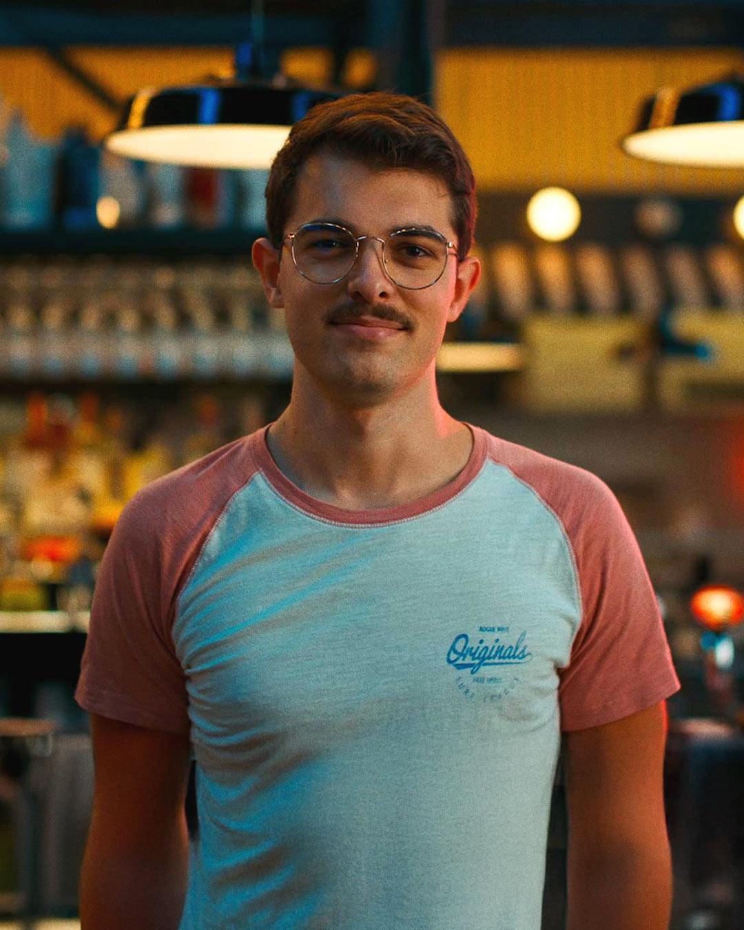 Portrait d'un jeune homme avec lunettes filmé au téléobjectif dans un bar, illustrant le flou d'arrière-plan et la profondeur de champ en vidéo professionnelle.