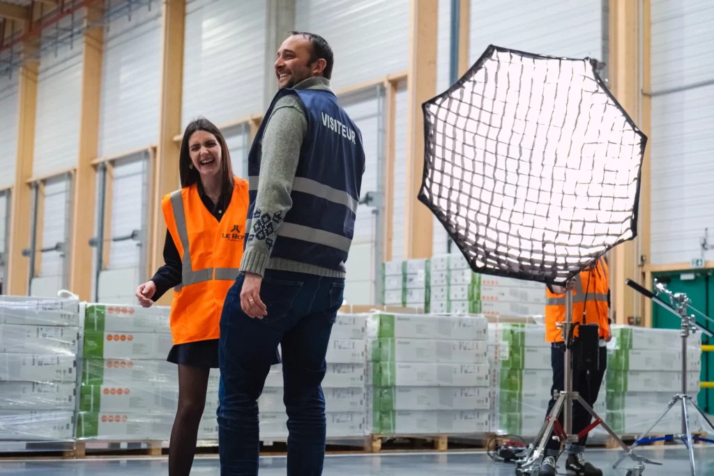 Deux collaborateurs posant près d’une grande source de lumière pendant le tournage dans l’entrepôt.