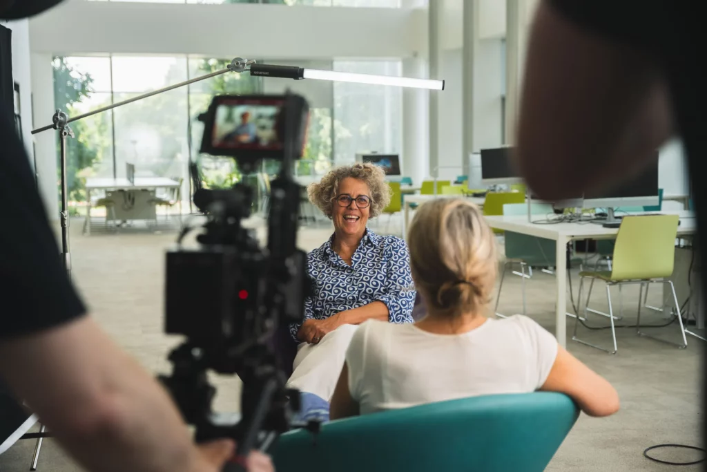 Caméra filmant une chercheuse pendant une interview dans un espace universitaire lumineux.