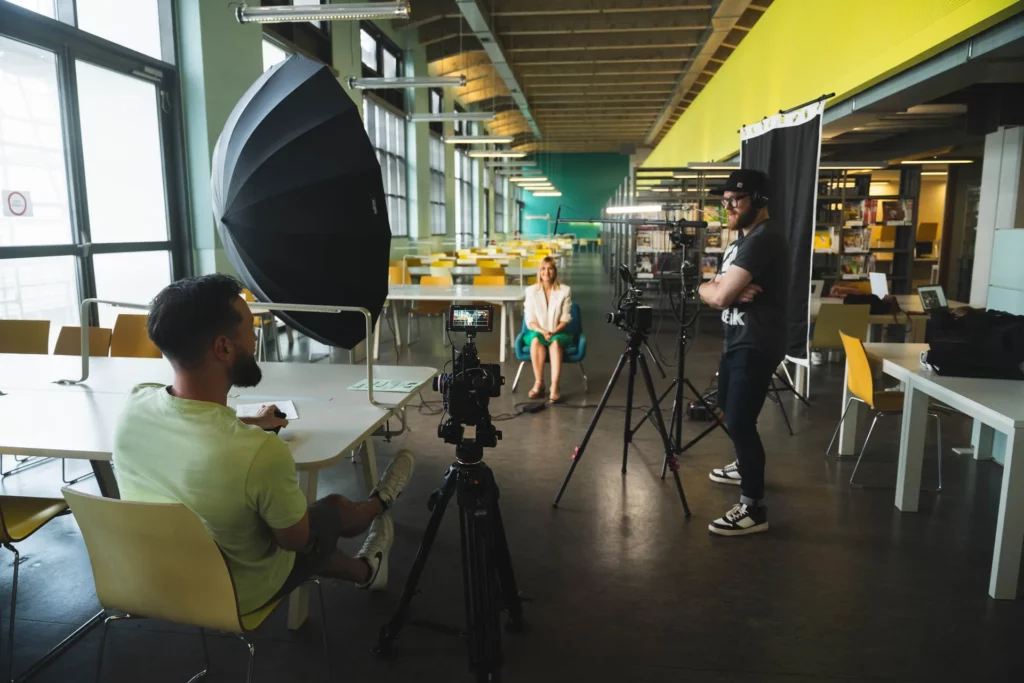 Équipe technique filmant une interview avec caméra, réflecteur et éclairage dans un espace universitaire.