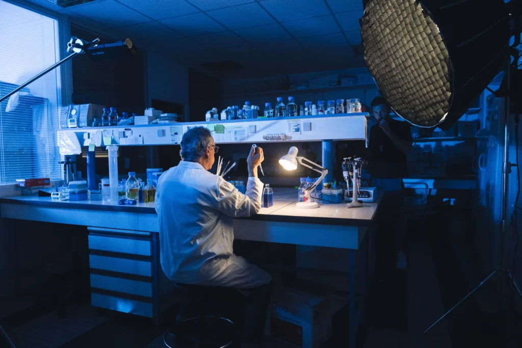 Chercheur filmé à son poste de travail dans un laboratoire éclairé en bleu.