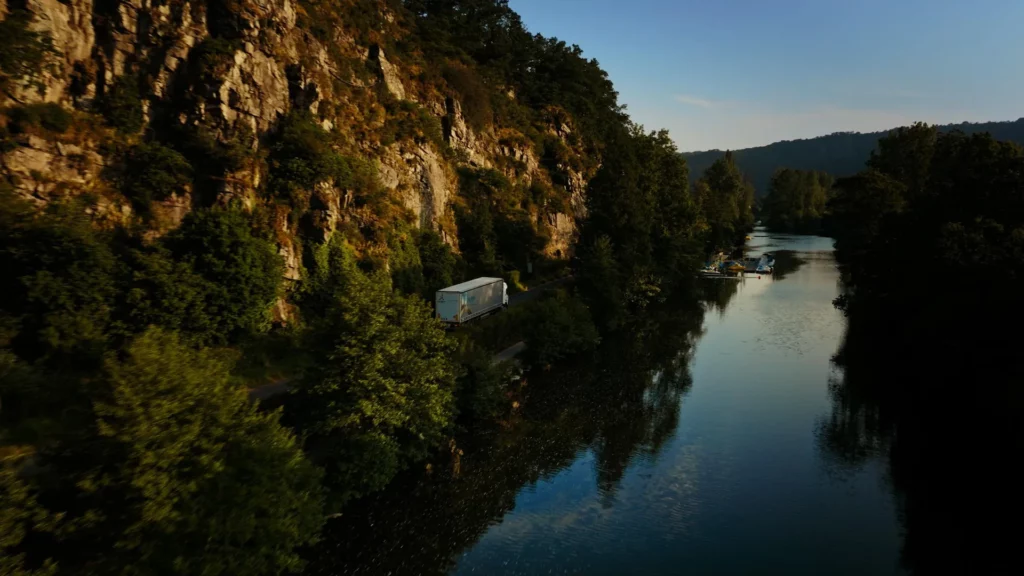 Camion Le Roy Logistique longeant une rivière entre falaises et végétation, dans une prise de vue aérienne.