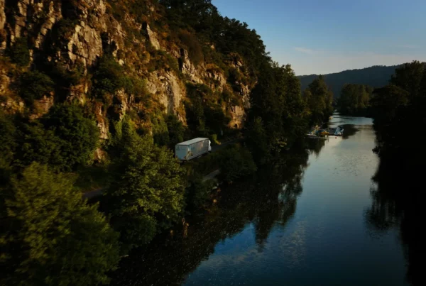 Camion Le Roy Logistique longeant une rivière entre falaises et végétation, dans une prise de vue aérienne.