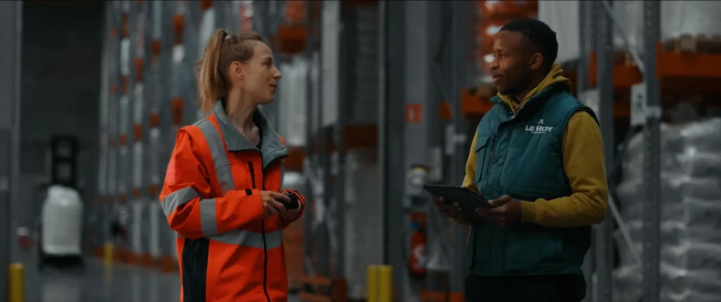 Deux collaborateurs Le Roy Logistique échangeant dans les allées d’un entrepôt de stockage.