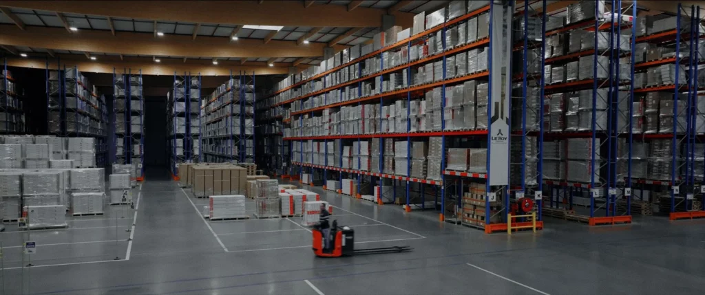 Vue générale d’un vaste entrepôt Le Roy Logistique avec rayonnages, palettes et engins de manutention.