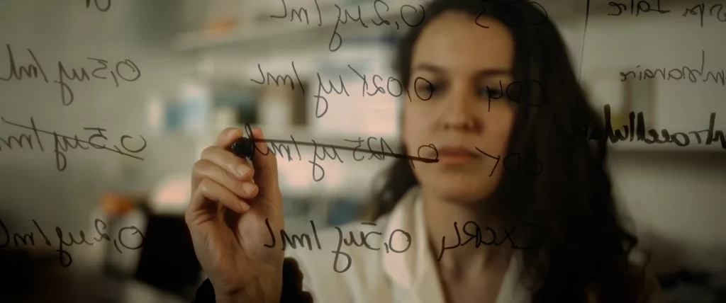 Chercheuse écrivant sur une paroi transparente pour illustrer un travail de recherche en psychologie.
