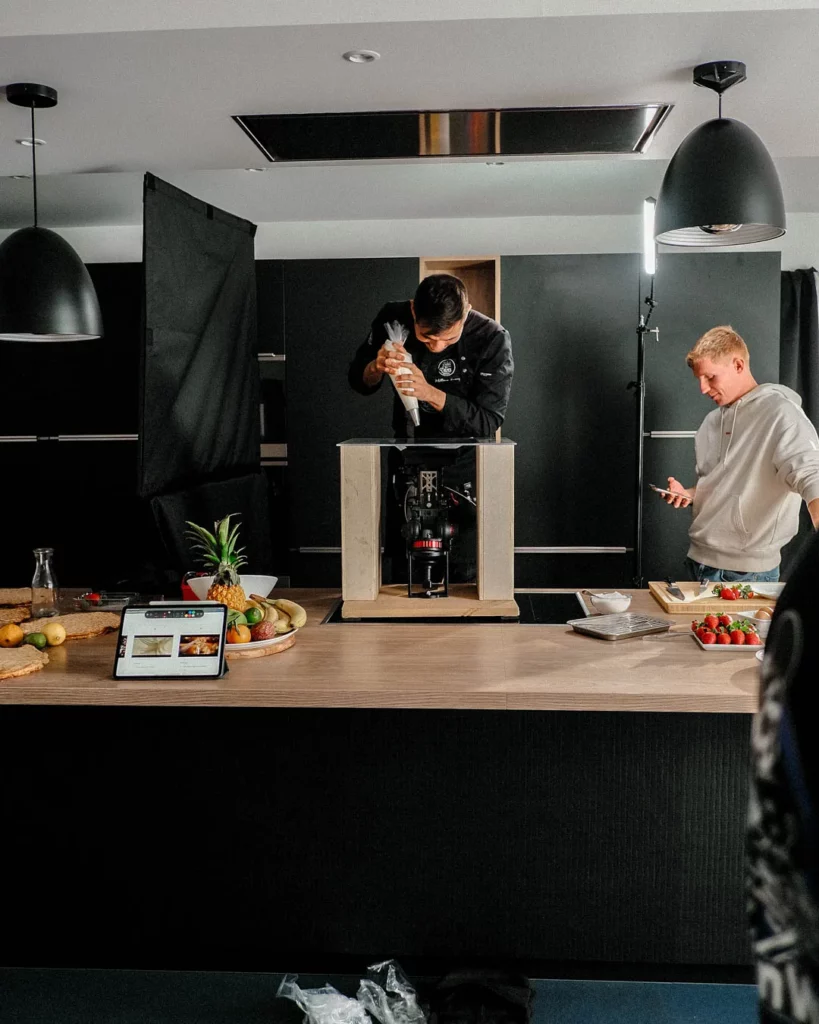 Équipe filmant un chef en cuisine derrière un îlot pendant la préparation d’une scène culinaire.