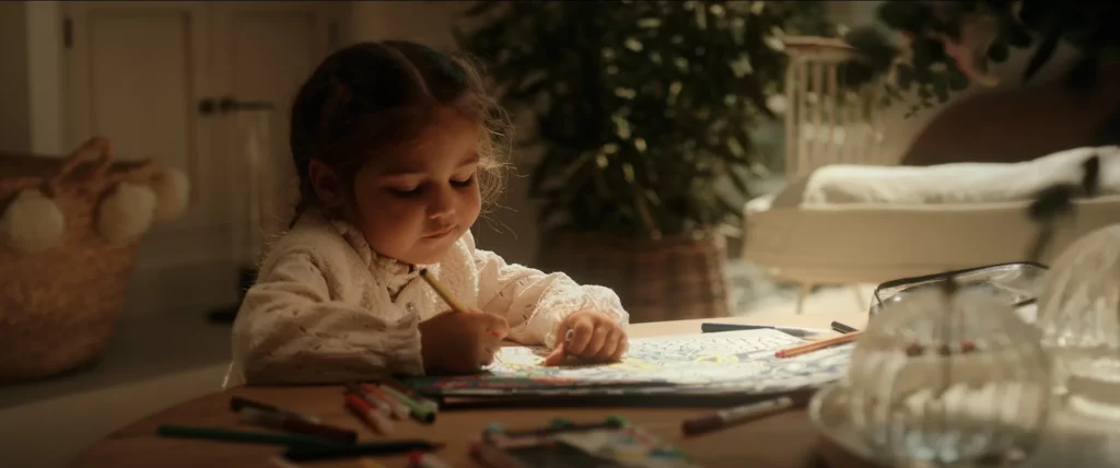 Enfant dessinant à une table dans un intérieur lumineux, près de la baie vitrée coulissante.
