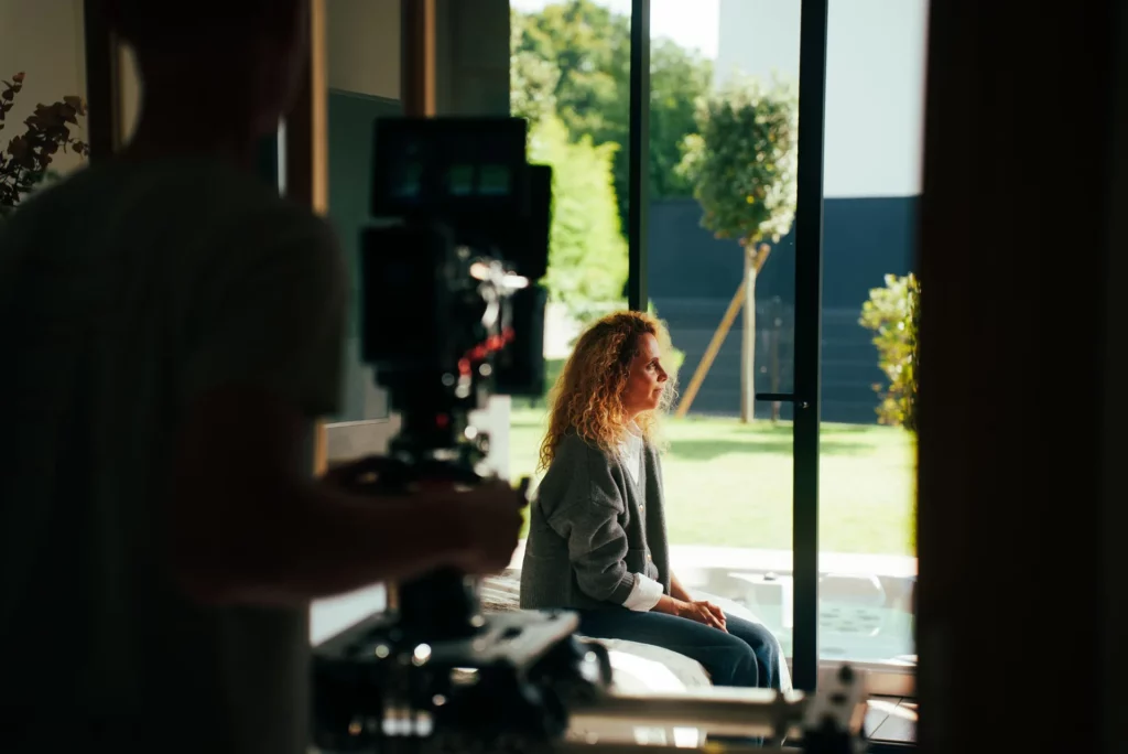 coulisses-campagne-bochassy-portrait-actrice Opérateur filmant une actrice assise près de la baie vitrée, avec le jardin en arrière-plan.