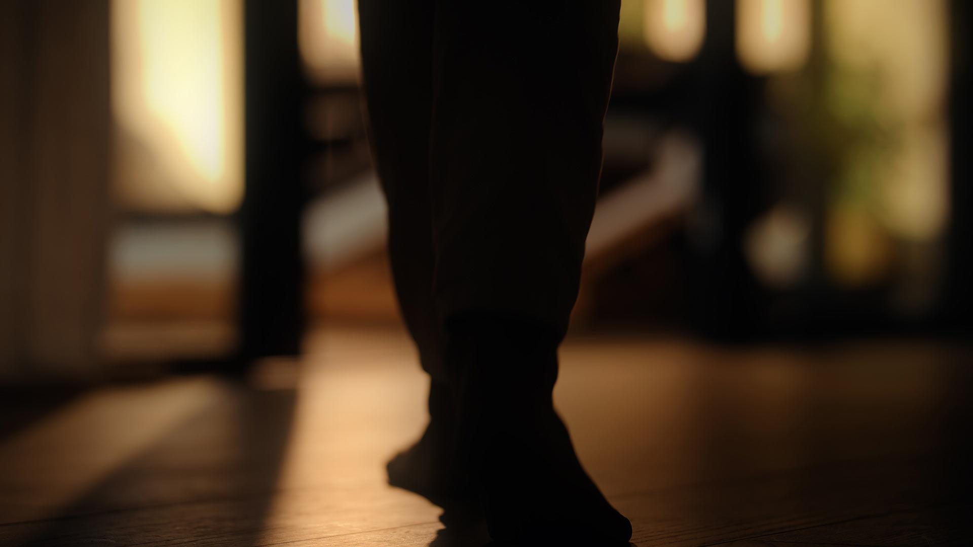 Gros plan sur les pieds franchissant le seuil d’une baie vitrée, éclairés par un rayon de lumière dorée qui renforce la sensation de chaleur.