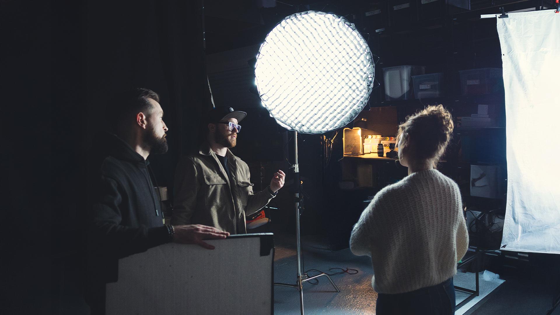Trois membres de l’équipe sur un plateau discutent devant une grande lumière LED et une toile de diffusion, illustrant la lumière utilisée comme un véritable langage visuel.