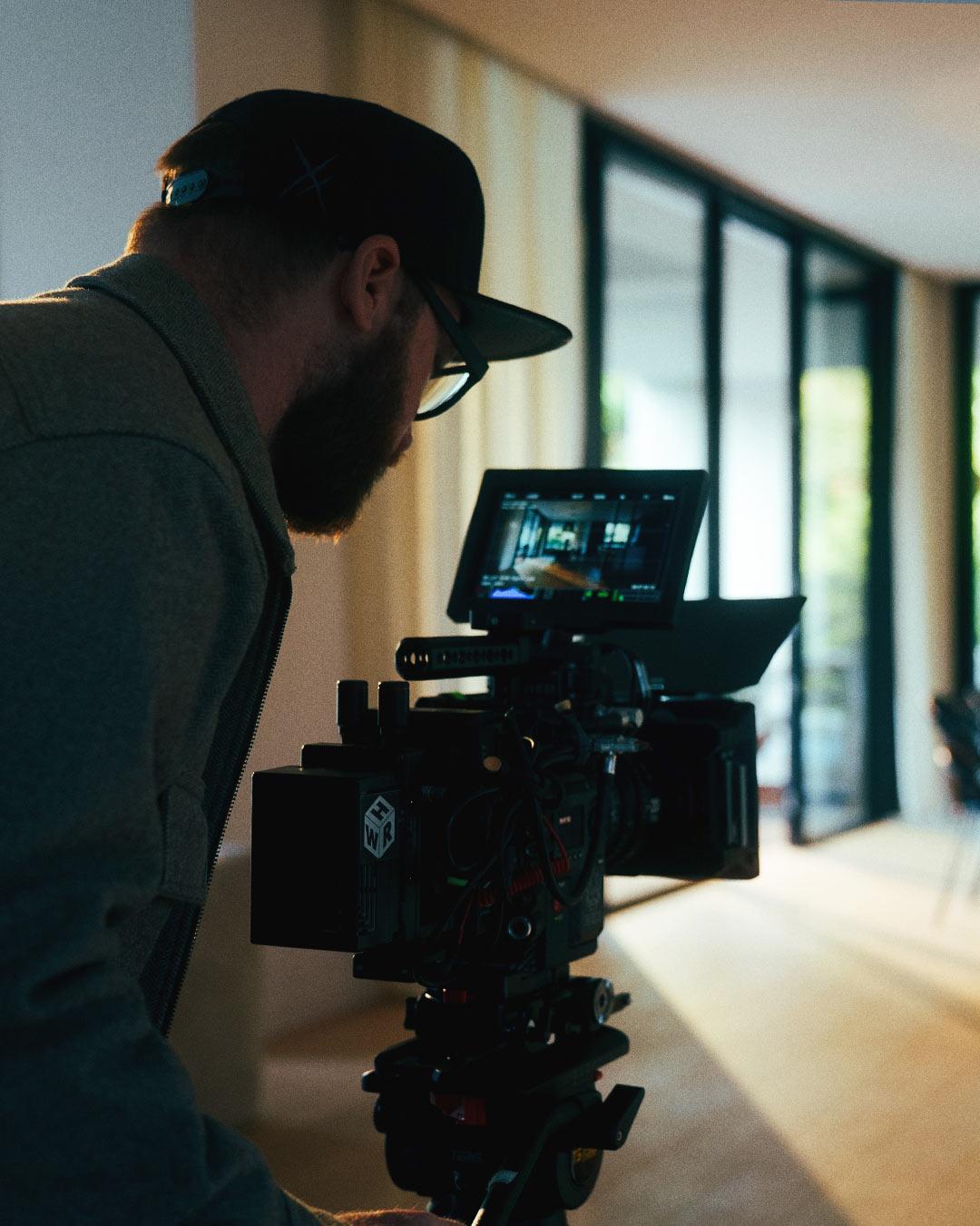 Robin Welschinger réglant une caméra cinéma sur un tournage vidéo en intérieur avec lumière naturelle, illustrant les coulisses d'une production.