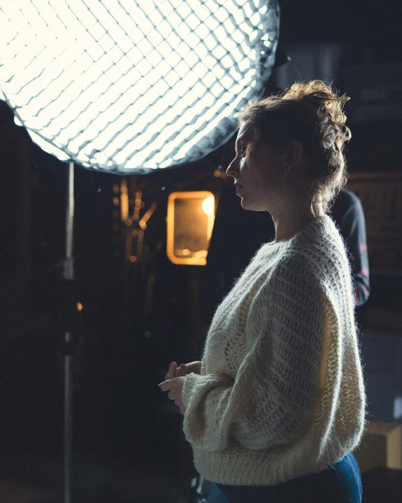 Portrait en contre-jour d’une femme face à une grande lampe LED ronde, symbole de la lumière comme véritable langage visuel sur le plateau.