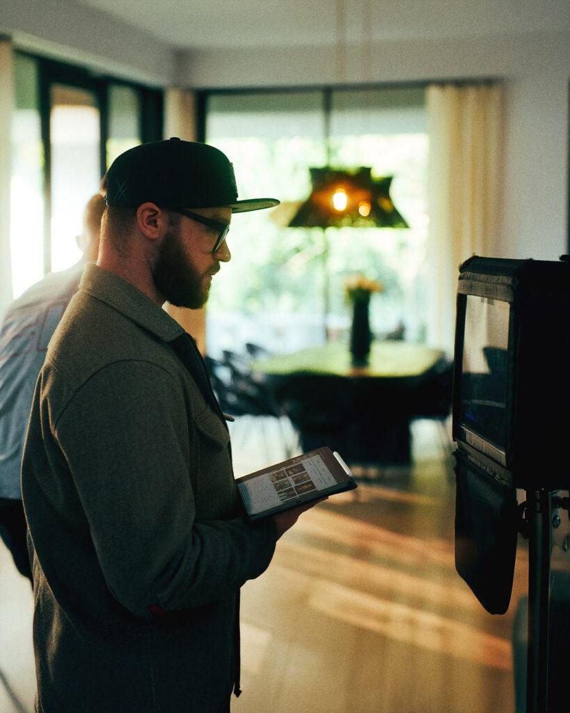 Robin Welschinger, chef opérateur, en pleine préparation de tournage avec un moniteur vidéo et un iPad, dans une ambiance lumineuse et chaleureuse.