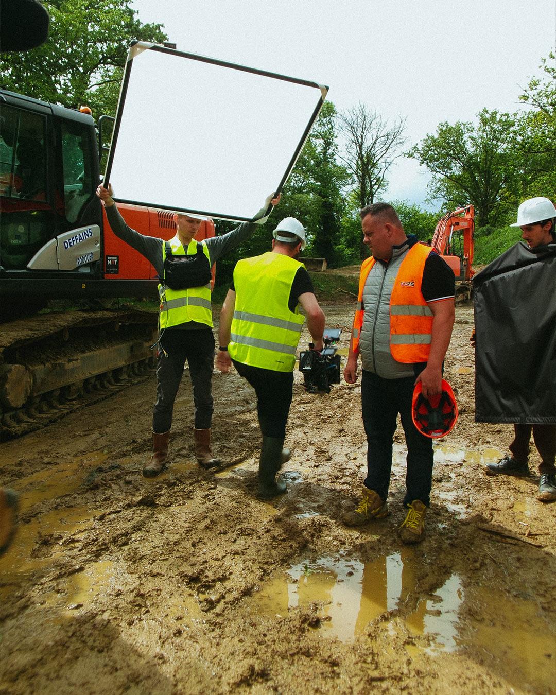 Tournage en conditions difficiles sur un chantier boueux pour un film Hitachi – lumière adoucie avec diffuseur et équipe technique sur le terrain