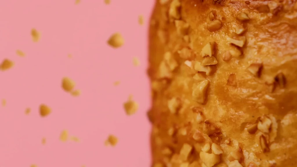 Très gros plan sur les éclats croustillants de la viennoiserie Signature Framboise Litchi sur un fond rose épuré.