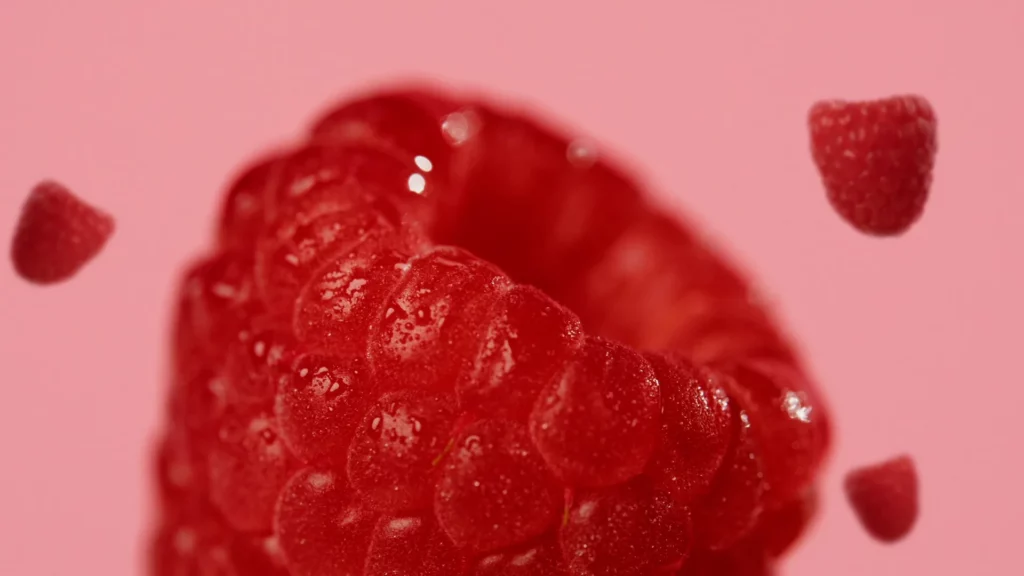 Macro d’une framboise brillante avec d’autres framboises floues autour, dans l’univers rose du film Bridor × Pierre Hermé.