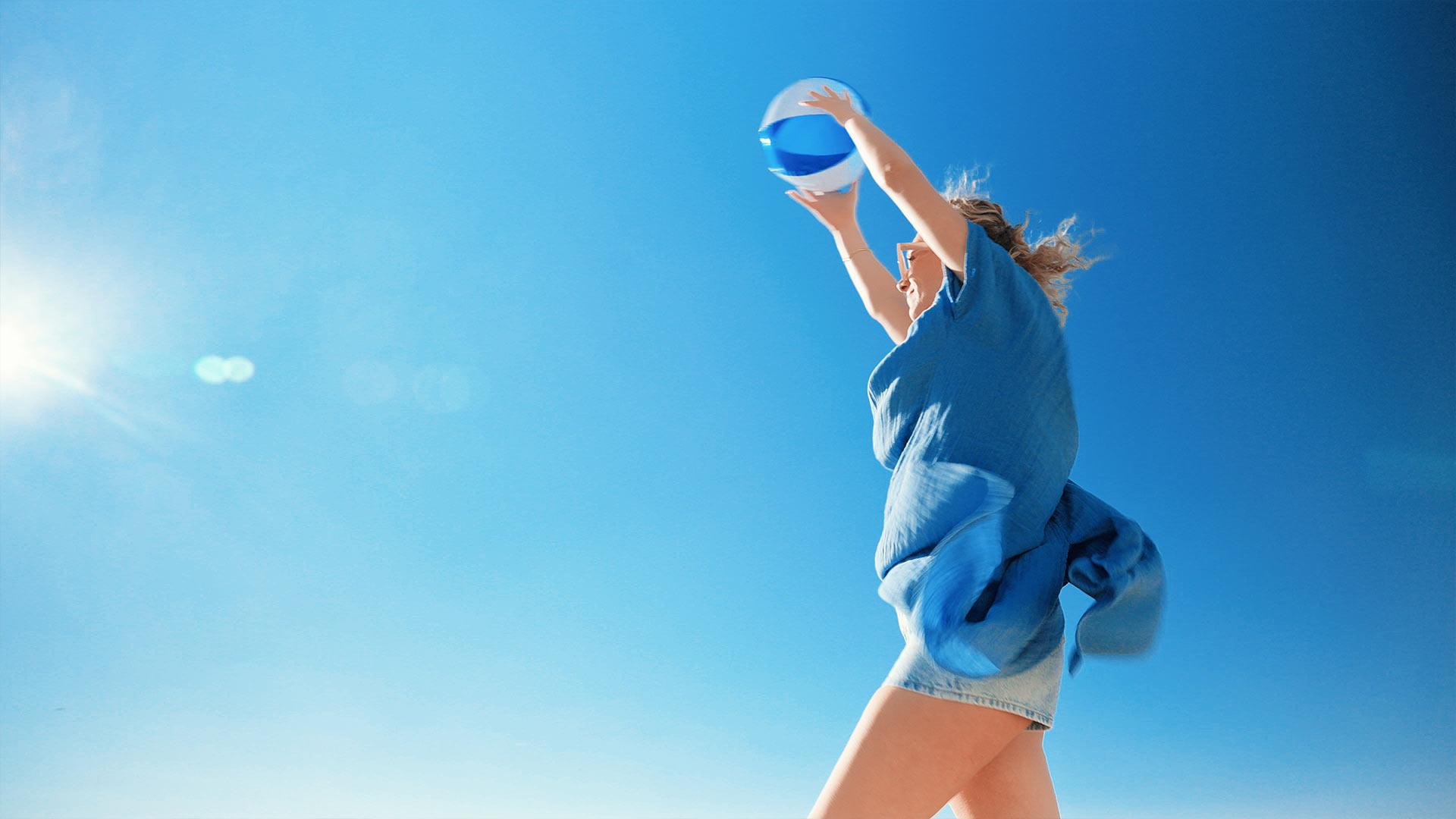 Plan serré sur une comédienne jouant avec un ballon de plage bleu sur fond de ciel d’hiver