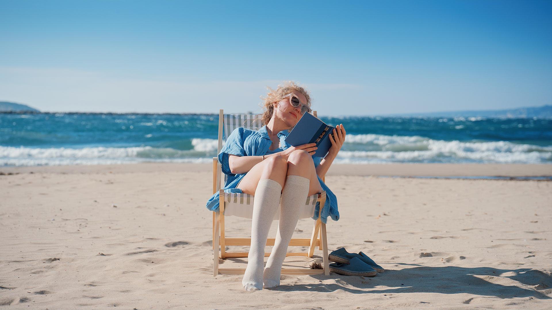 Portrait d’une femme lisant un livre sur une chaise de plage, éclairage dur pour simuler un soleil d’été