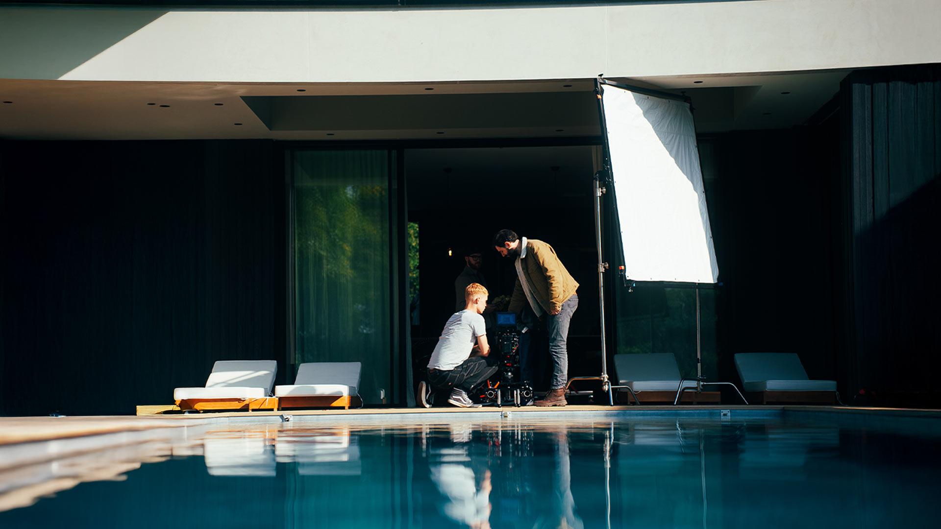 Équipe de tournage en extérieur près d'une piscine avec réflecteur et caméra, lors d'une production vidéo réalisée par Robin Welschinger.