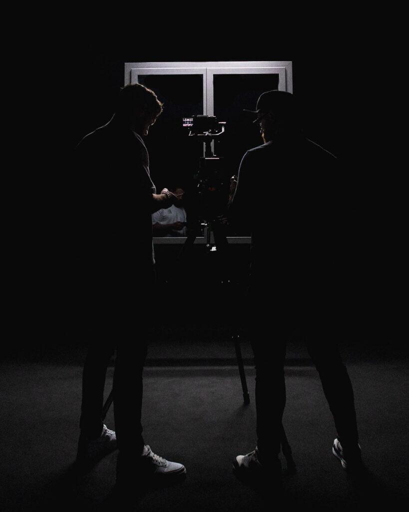 Silhouettes de deux vidéastes devant une caméra en contre-jour, illustrant la dualité entre réalisation et image