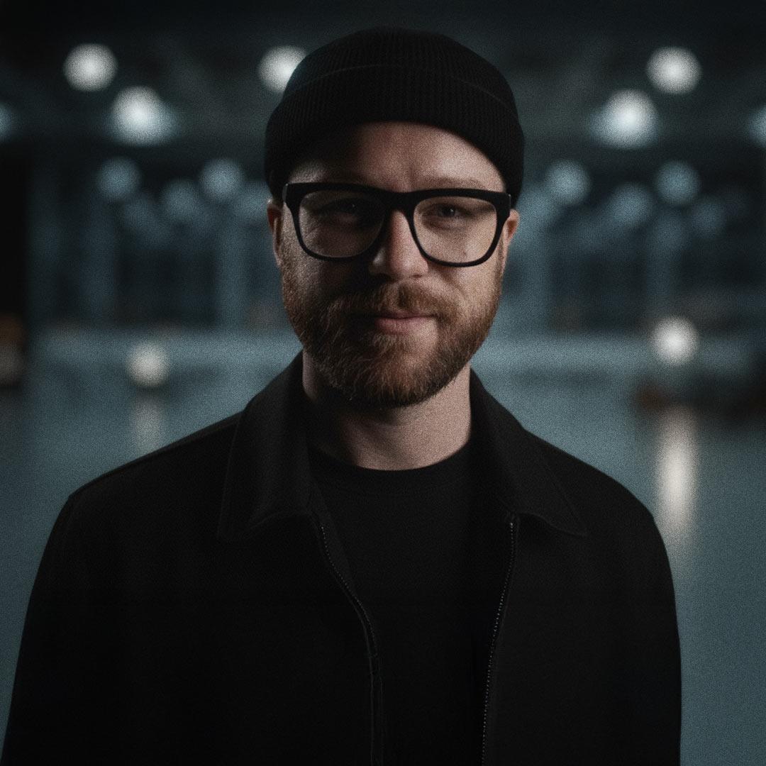 Portrait cinématographique en studio de Robin Welschinger, vidéaste à Rennes avec bonnet et lunettes, regard caméra, fond flou.