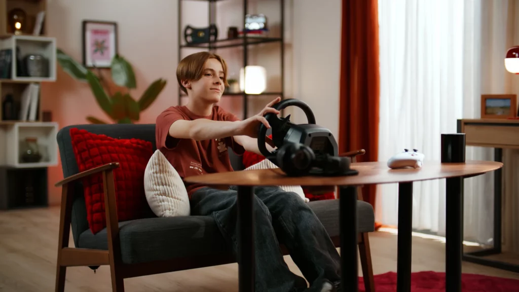 Jeune joueur installé à une table avec le volant gaming Thrustmaster T98 dans un décor lifestyle lumineux.