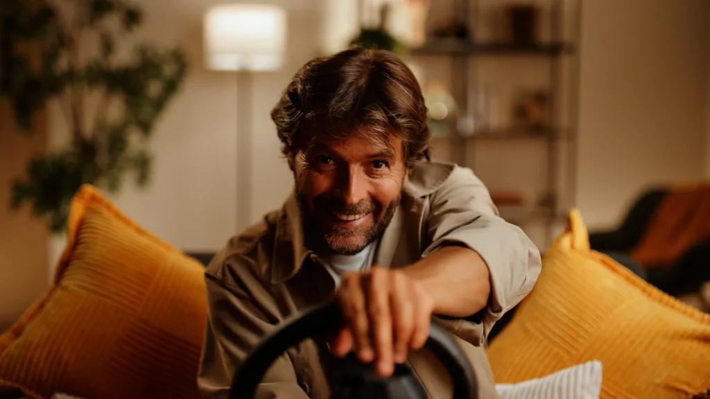 Joueur souriant en pleine partie avec le volant gaming Thrustmaster T98 dans une ambiance lumineuse.