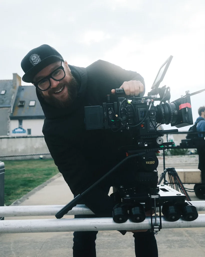 about-bts-chef-operateur-camera-exterieur Chef opérateur souriant derrière une caméra cinéma installée en extérieur.