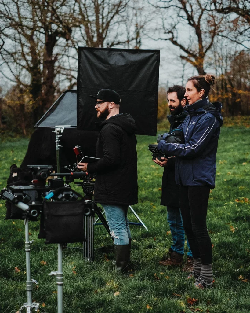 about-bts-equipe-camera-tournage-nature Équipe technique regroupée autour d’une caméra lors d’un tournage en extérieur dans un environnement naturel.