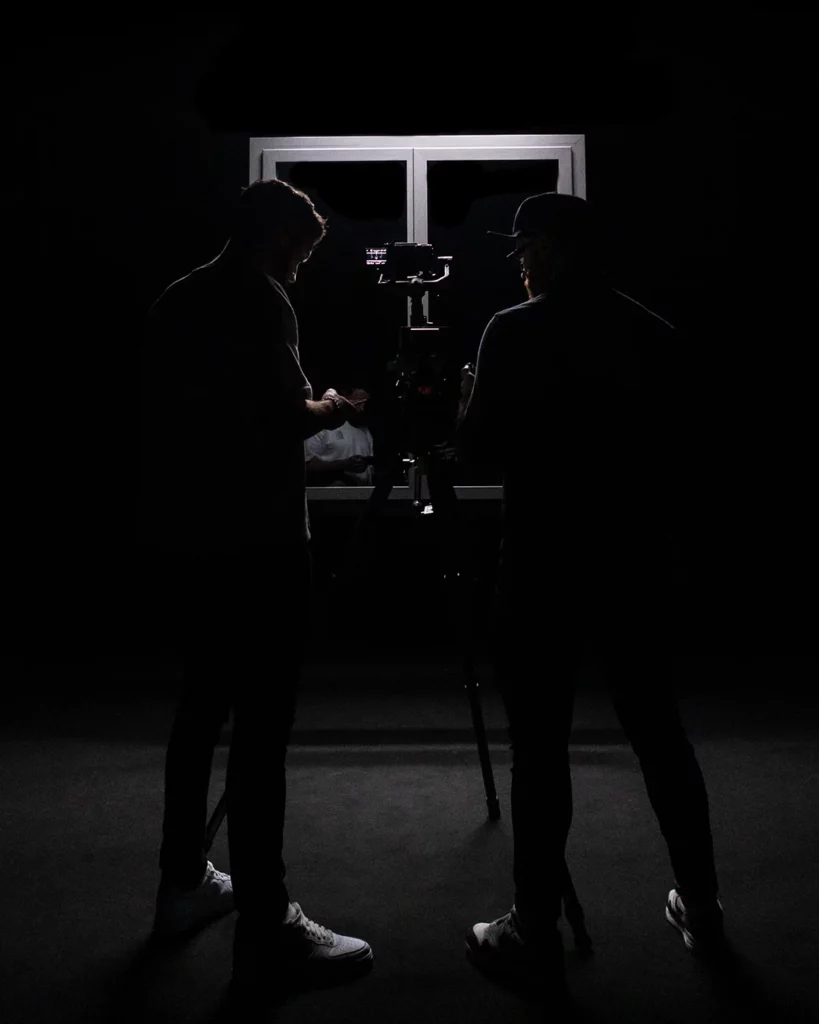 about-bts-equipe-moniteur-plateau-sombre Deux membres de l’équipe observant un moniteur sur un plateau sombre pendant le tournage.