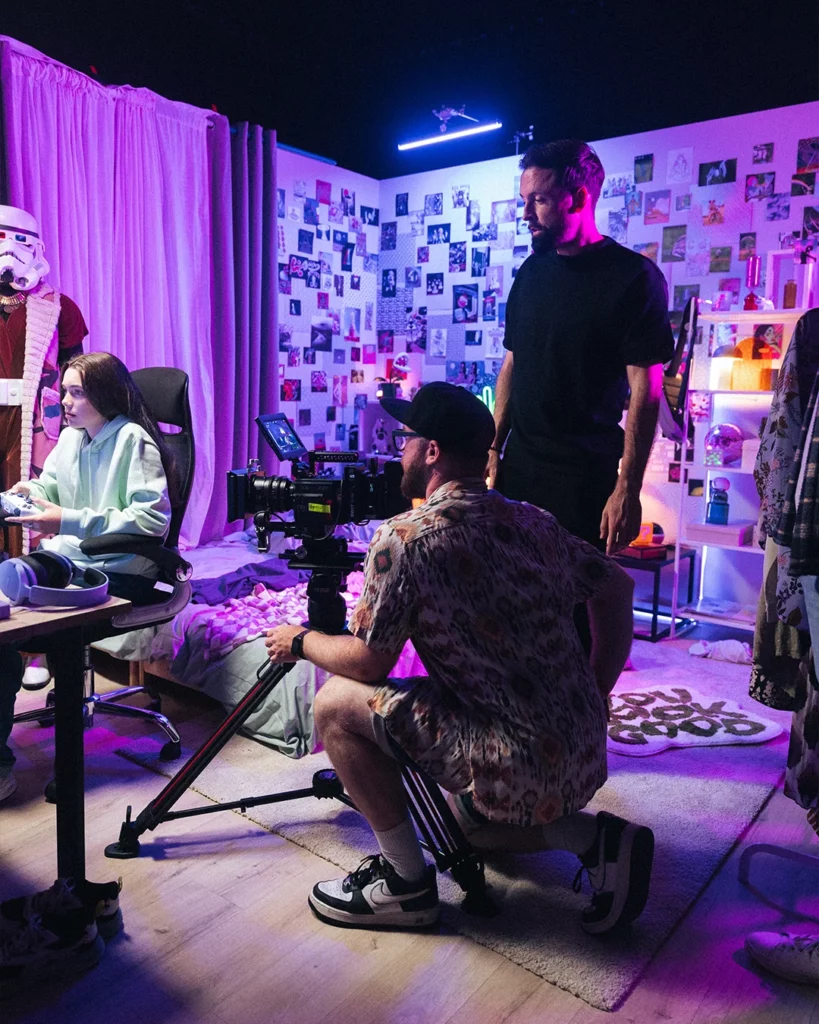 about-bts-equipe-plateau-studio-colore Équipe de tournage au travail dans un décor studio coloré avec caméra et éclairage.