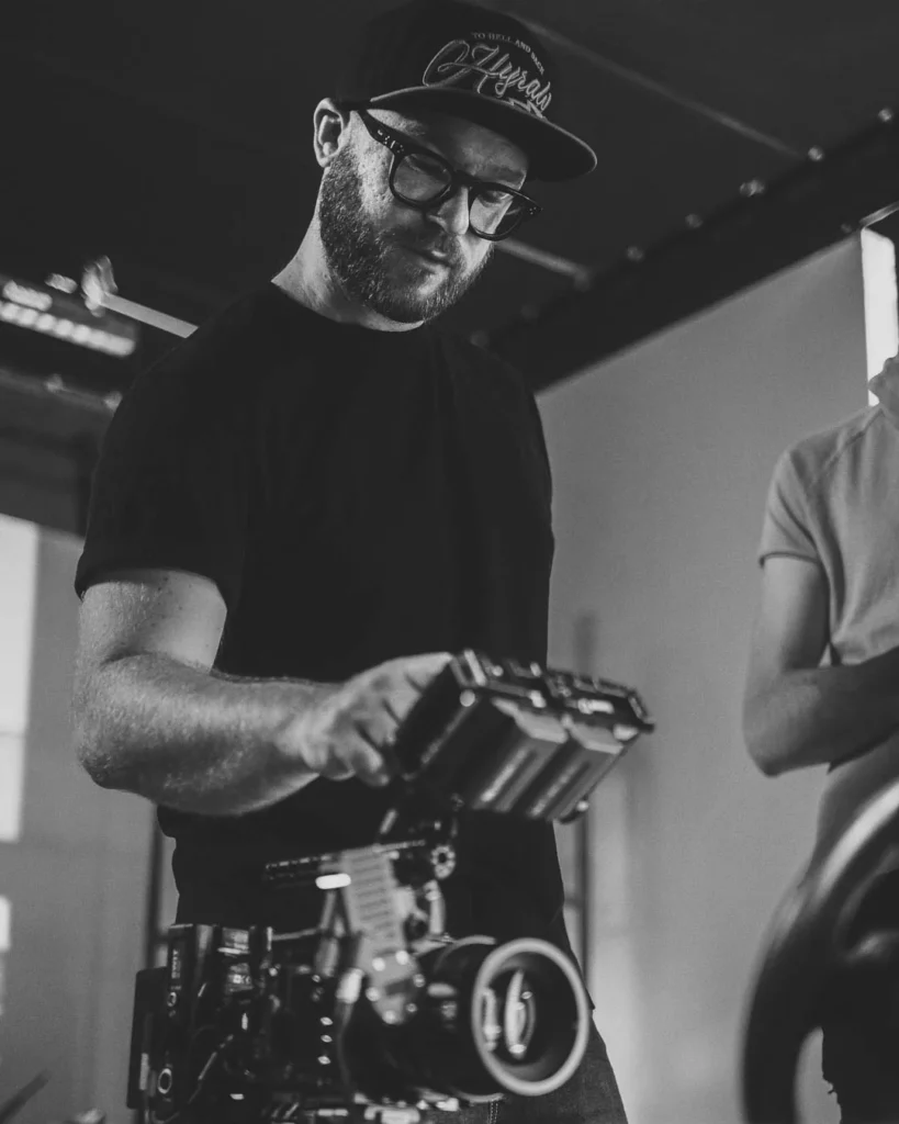 about-bts-reglage-camera-noir-et-blanc Technicien réglant une caméra cinéma dans une image de coulisses en noir et blanc.