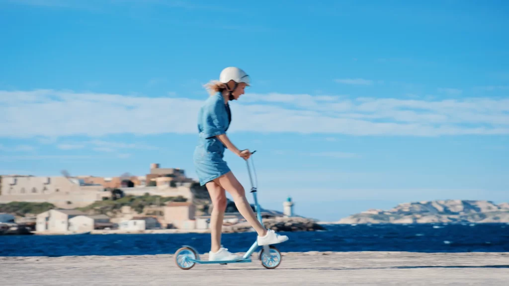 about-slider-publicite-femme-trottinette-bord-mer Femme avançant en trottinette au bord de la mer dans une scène publicitaire lumineuse et dynamique.