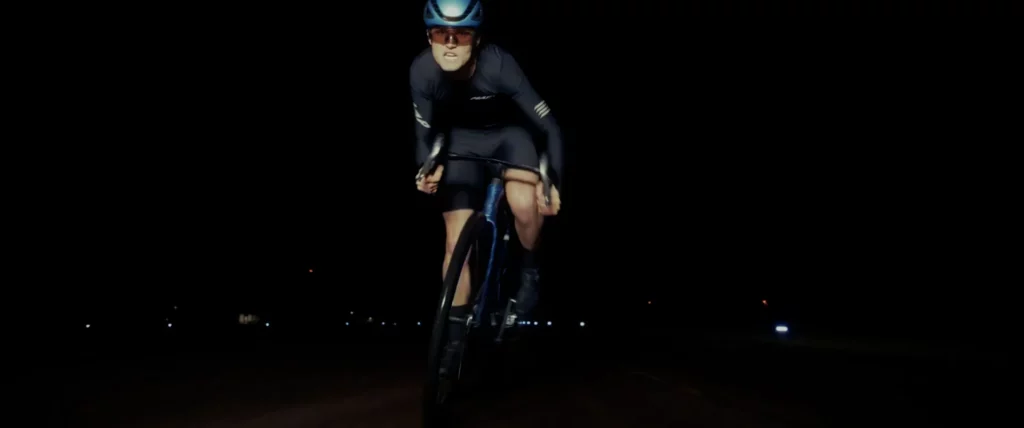 Cycliste roulant vers la caméra sur une piste d’aéroport, éclairé de face dans une ambiance nocturne.
