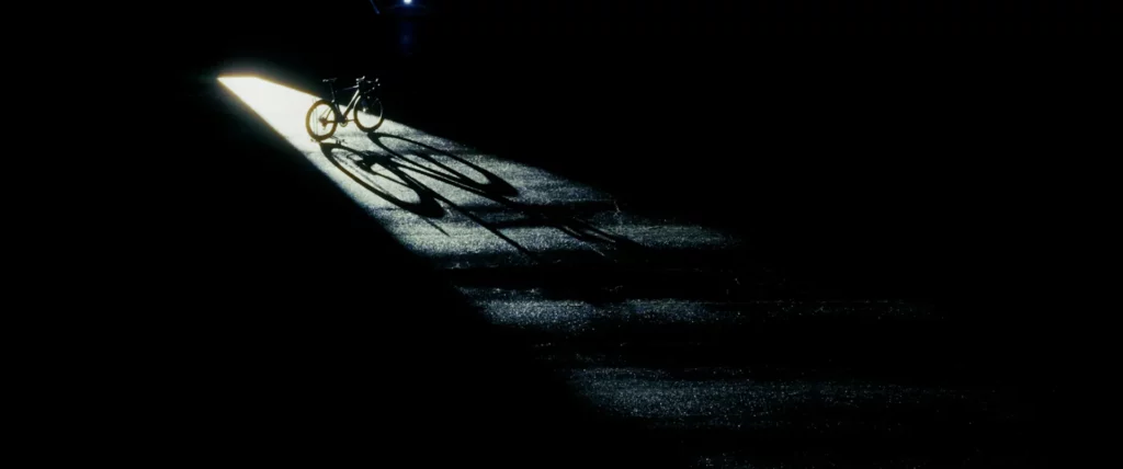 Ombre d’un cycliste projetée par un faisceau lumineux sur une piste d’aéroport de nuit.