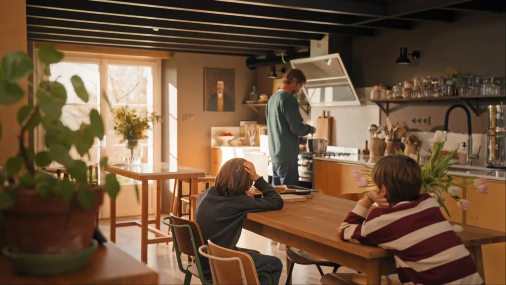 Arnaud préparant le repas pendant que les enfants sont assis autour de la table Jonàk dans la cuisine.