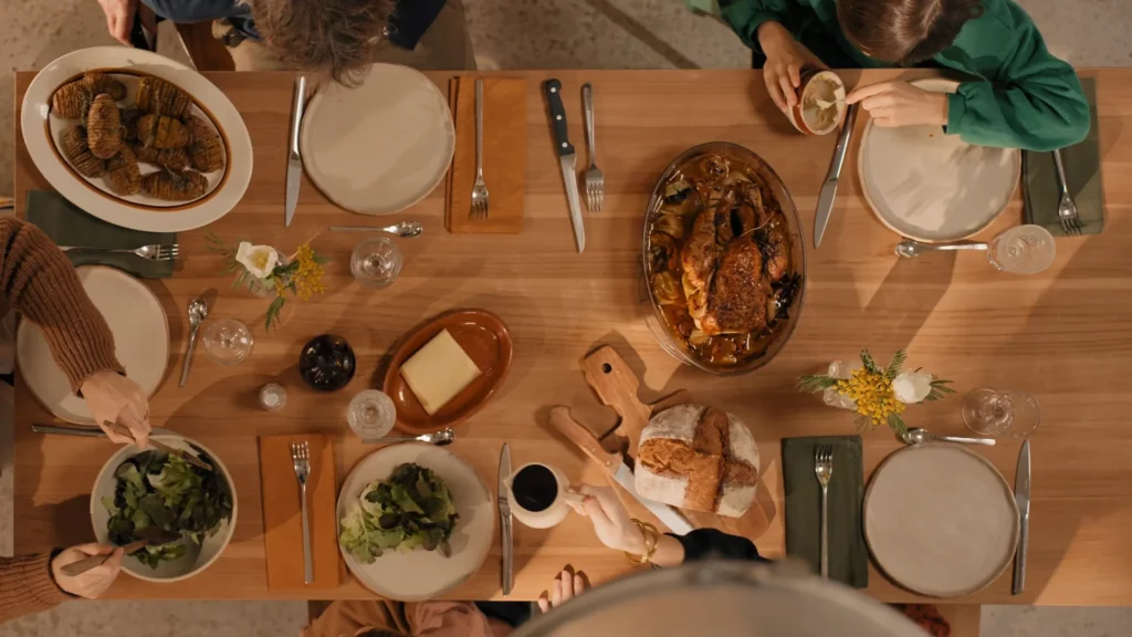 Famille réunie autour de la table Jonàk de Tikamoon pour un repas dans une maison lumineuse.