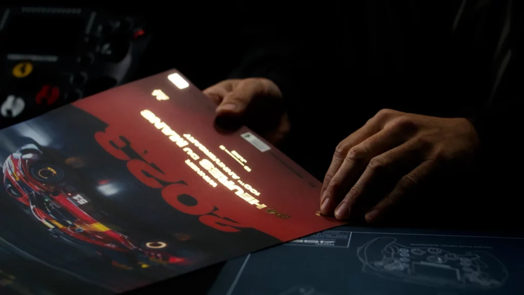 Mains consultant les documents de collection Ferrari 499P posés près du volant Thrustmaster.