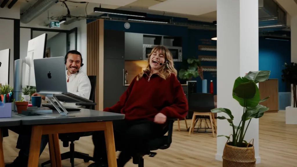 Conseillère souriante dans l’open space avec un collègue à son poste dans Flexible Contact Center