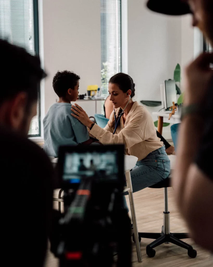2026-ydeo-ensemble-formulons-votre-avenir-bts-consultation-camera-enfant Coulisses d’une scène de consultation du film YDEO, avec une femme au stéthoscope examinant un enfant devant la caméra.