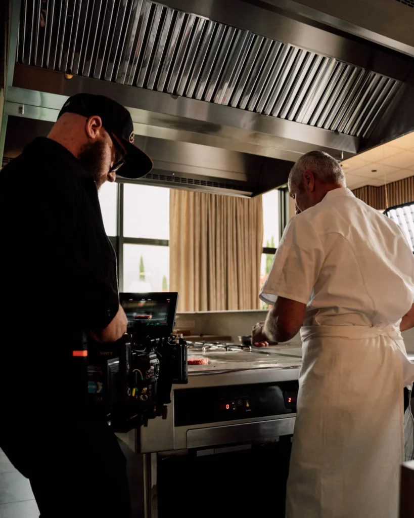 2026-ydeo-ensemble-formulons-votre-avenir-bts-cuisine-camera-tournage Coulisses du tournage YDEO dans une cuisine professionnelle, avec un opérateur caméra filmant un homme en tenue blanche au plan de travail.