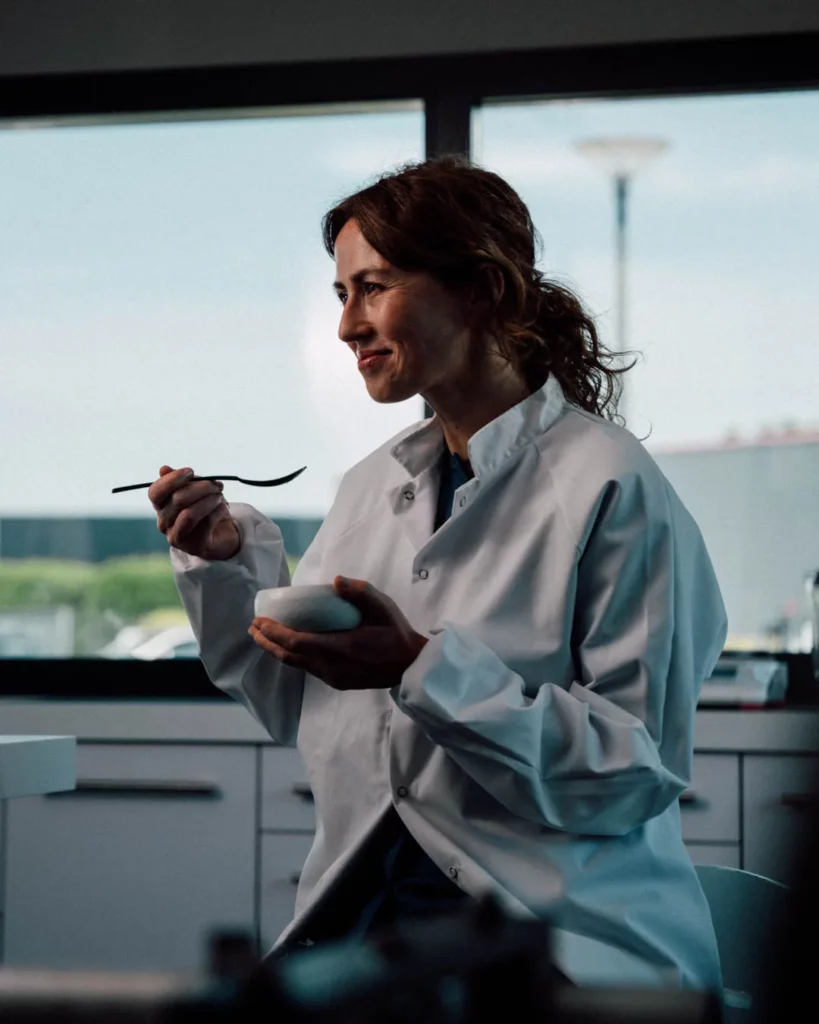2026-ydeo-ensemble-formulons-votre-avenir-bts-laboratoire-femme-blouse Femme en blouse blanche tenant un bol et une cuillère dans un laboratoire pendant le tournage du film YDEO Ensemble, formulons votre avenir.