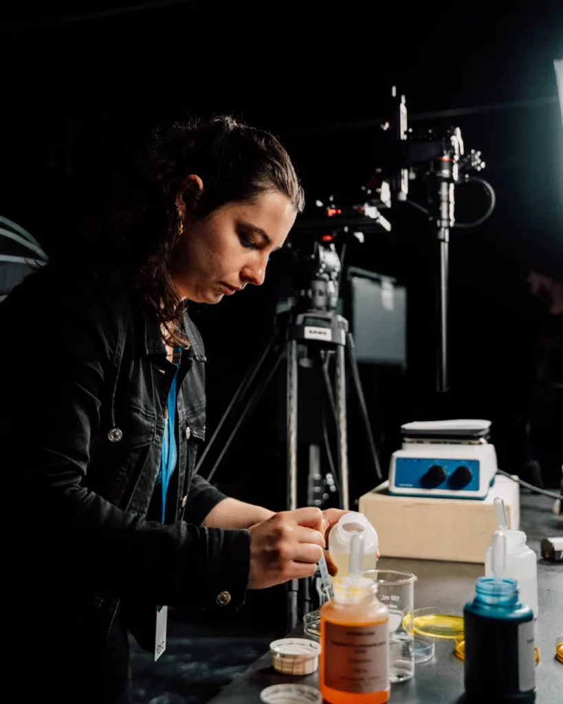 2026-ydeo-ensemble-formulons-votre-avenir-bts-laboratoire-preparation-accessoires Coulisses du tournage YDEO en laboratoire, avec une femme préparant des liquides colorés devant le matériel de prise de vue.