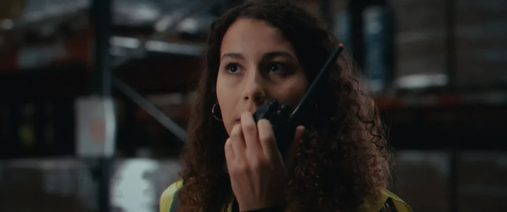 Opératrice en gilet haute visibilité utilisant un talkie-walkie dans un entrepôt, scène du film YDEO Ensemble, formulons votre avenir