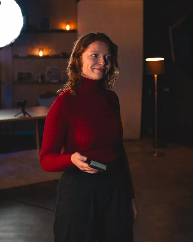 Portrait d’une femme debout sur un plateau studio, éclairée dans une ambiance plus contrastée.