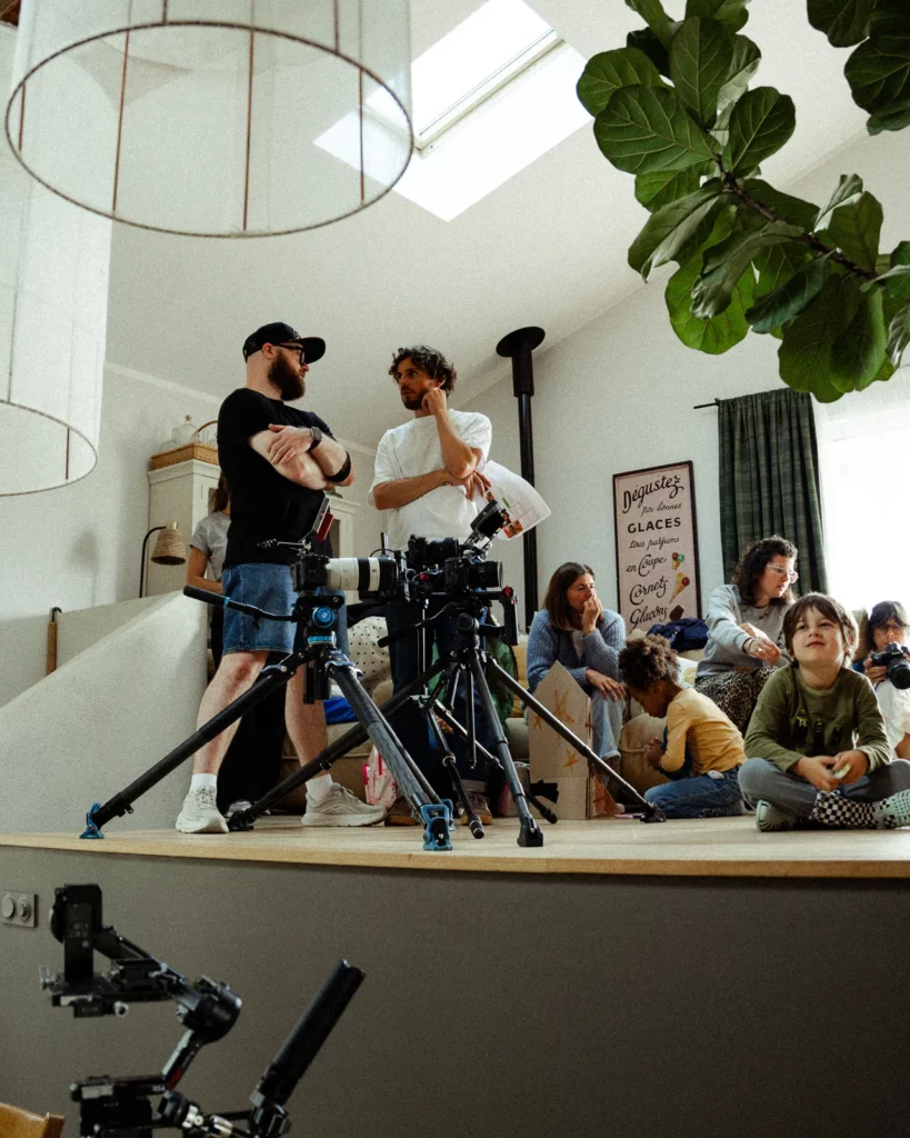lunii-bts-cameras-trepieds-equipe-preparation-2026 Deux caméras sur trépieds et plusieurs membres de l'équipe autour du décor pendant la préparation d'une prise pour Lunii.