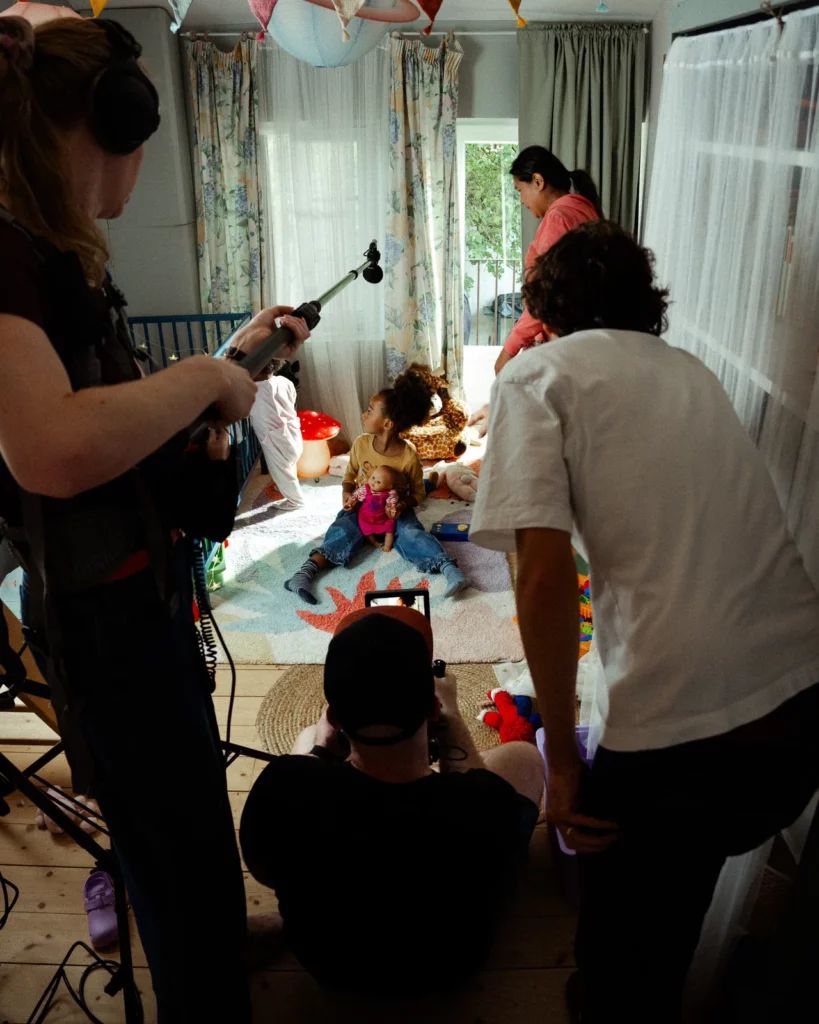 lunii-bts-equipe-filme-enfants-chambre-perche-2026 Vue des coulisses Lunii : des techniciens filment deux enfants dans une chambre avec une caméra basse et une perche son.
