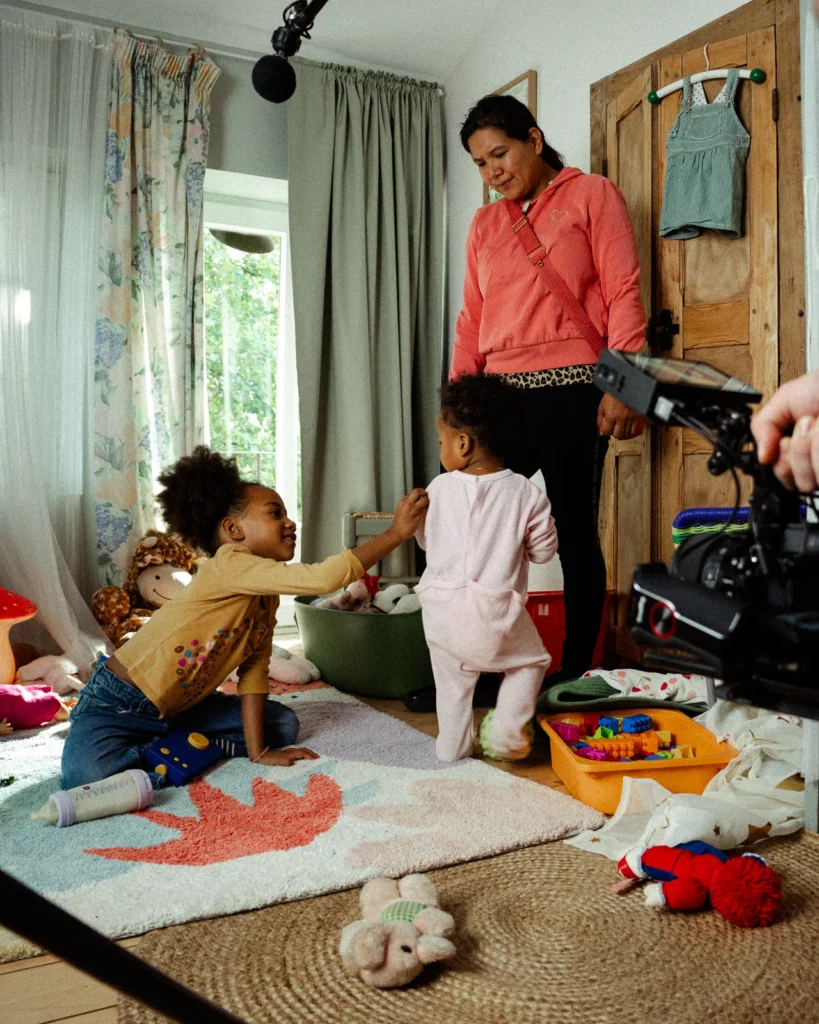 lunii-bts-tournage-enfants-camera-perche-son-2026 Sur le plateau Lunii, deux enfants jouent près d'une adulte tandis qu'une caméra et une perche son encadrent la scène.
